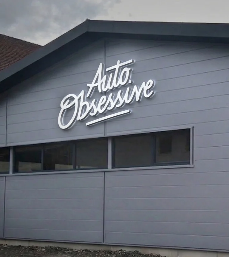 Enseigne en lettres relief blanches « Auto Obsessive » sur façade en bardage gris